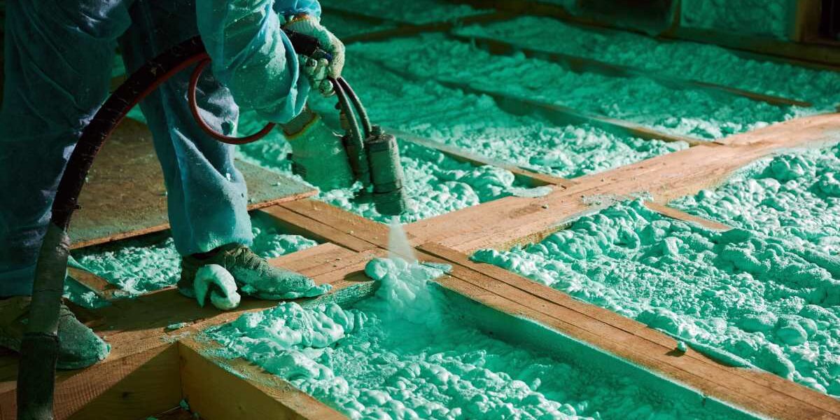 man using a machine to spray foam insulation in a wooden attic