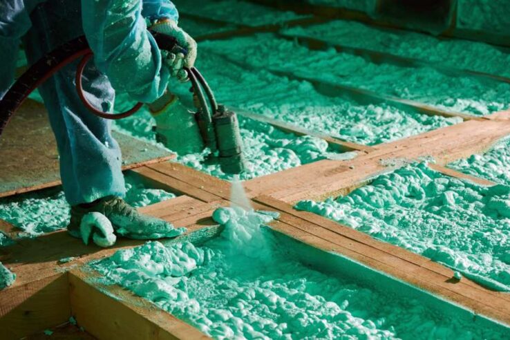 man using a machine to spray foam insulation in a wooden attic